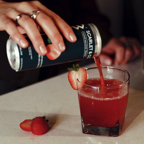 Person pouring Nasdrow Scarlet & Co mocktail into a glass, garnished with fresh strawberries.